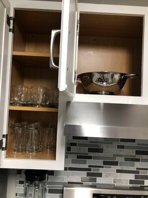 A kitchen with a white cabinet containing clear drinking glasses and a stainless steel colander. - RARE - 2 miles to Dollywood - Arcades & Much More (Sevierville)