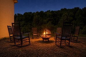 A fire pit with four chairs arranged around it, set on gravel, with a forested background. - RARE - 2 miles to Dollywood - Arcades & Much More (Sevierville)