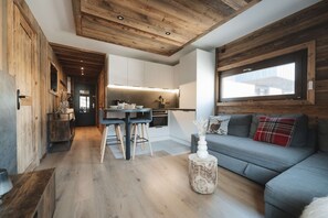 Ein modernes Interieur mit Holzbalkendecke, einer Küchenzeile, einem Esstisch mit Stühlen und einer Couch mit Kissen.
