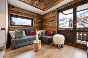 A cozy living room with a grey sectional sofa, a wooden coffee table, and a fluffy white pouf.