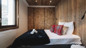 Ein Schlafzimmer mit einem großen Bett, Holzwänden, einem Fenster und Blick ins Freie.
