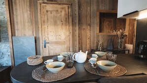 Ein Esstisch mit Schüsseln, Tassen, einem Teekessel und Gläsern, im Hintergrund eine Holztür und rustikale Dekoration.