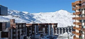 A modern hotel with multiple floors, balconies, and a snowy mountain backdrop.