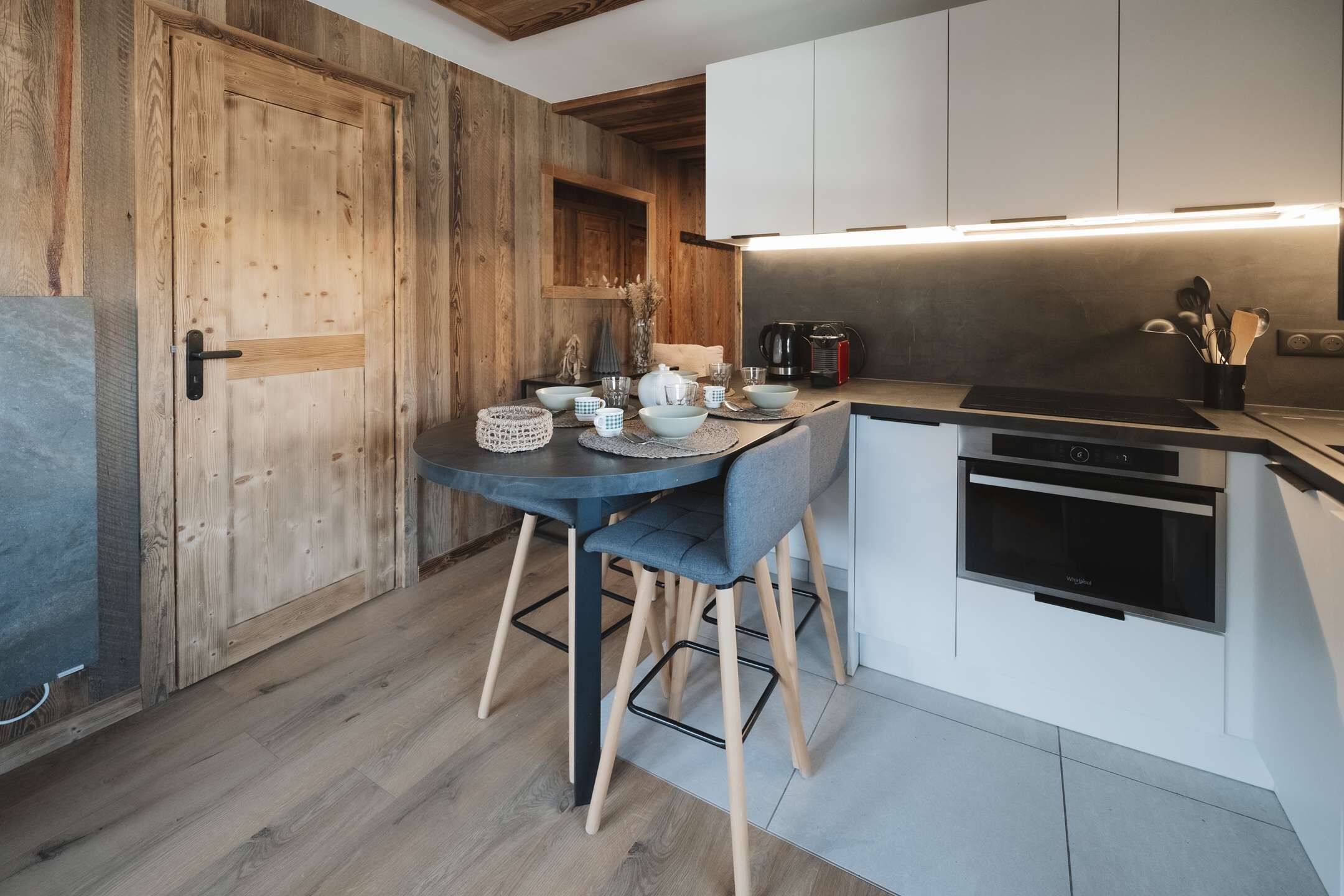 Eine moderne Küche mit Holztür, einem Esstisch mit Stühlen und einem eingebauten Backofen.
