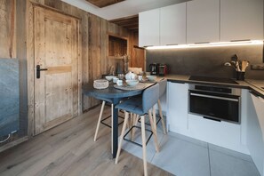 A modern kitchen with a wooden door, a dining table with chairs, and a built-in oven.
