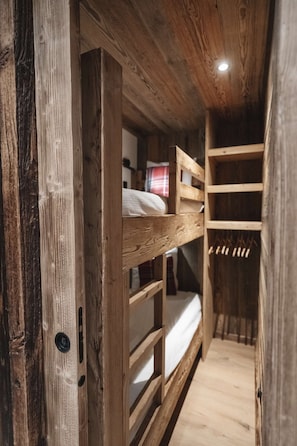 A wooden bunk bed with a ladder, a white mattress, and a wooden floor.