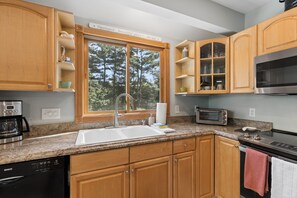 A kitchen with wooden cabinets, a sink, a microwave, a toaster, and a coffee maker. - Walk to Downtown OGT! (Ogunquit)