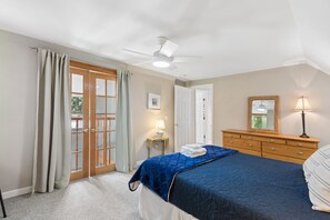 A bedroom with a bed, a dresser, a ceiling fan, and a door with glass panels.