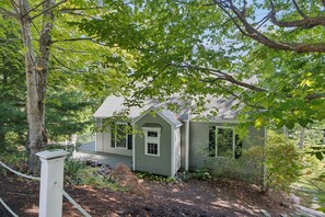 A single-story house with a gabled roof, surrounded by trees and a garden.