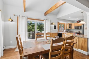 A spacious dining area with a wooden table and chairs, a kitchen with modern appliances, and a view of the outdoors through large sliding doors. - Walk to Downtown OGT! (Ogunquit)