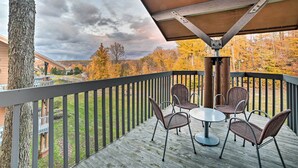 Eine Holzdielen-Terrasse mit Tisch und Stühlen, mit Blick auf eine Rasenfläche und Herbstbäume.