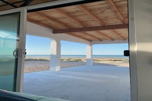 A beachside patio with a wooden ceiling and large windows overlooking the beach.