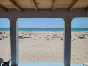 A beach view from a covered area with concrete pillars and a wooden ceiling.