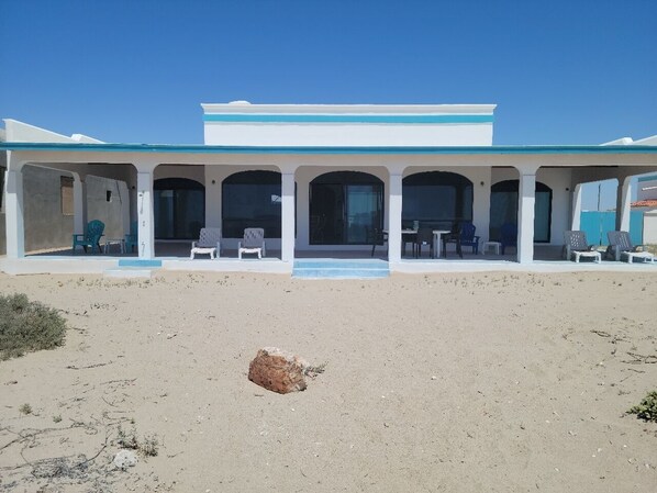 Un bâtiment situé en bord de mer, doté d’un patio couvert et d’un espace extérieur aménagé pour s’asseoir.