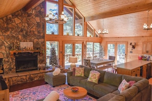 A cozy cabin interior with a stone fireplace, wooden walls, and a dining area with a view of the forest.