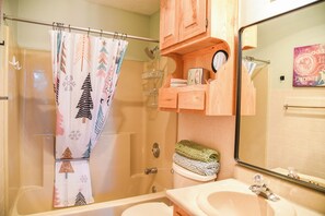 A bathroom with a shower curtain, a toilet, a sink, and wooden cabinets.