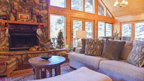 L’intérieur chaleureux d’un chalet avec une cheminée en pierre, un canapé, une table ronde et un sapin de Noël.
