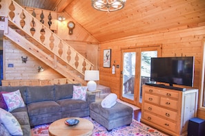 A wooden cabin interior with a sofa, ottoman, TV, and a staircase.