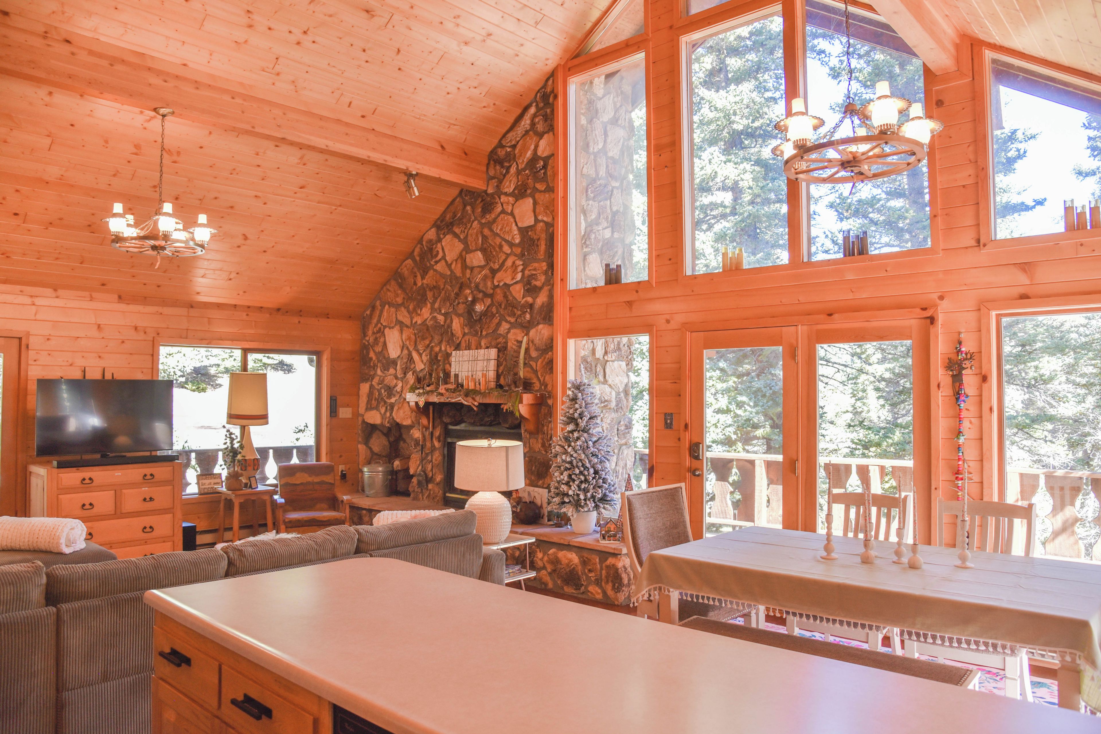 A cozy cabin interior with a stone fireplace, wooden walls, a television, and a dining area.