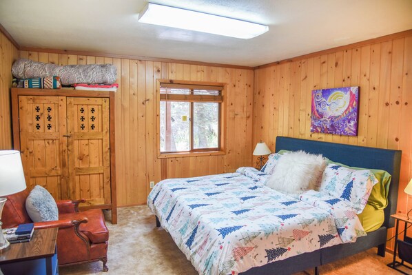 A wooden-paneled room with a bed, a desk, a chair, and a window.