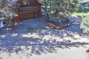 A wooden cabin with a balcony, surrounded by trees and a gravel driveway.