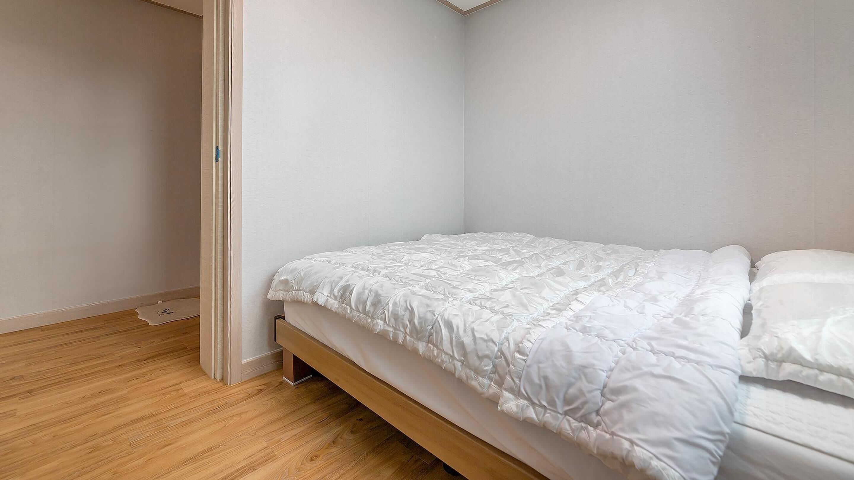 A small, neatly arranged bedroom with a single bed, wooden flooring, and white walls.