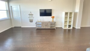 A spacious living room with hardwood flooring, a mounted TV, a wooden console table, and a white shelving unit. - Beautiful Lake House in Garland Texas (Garland)