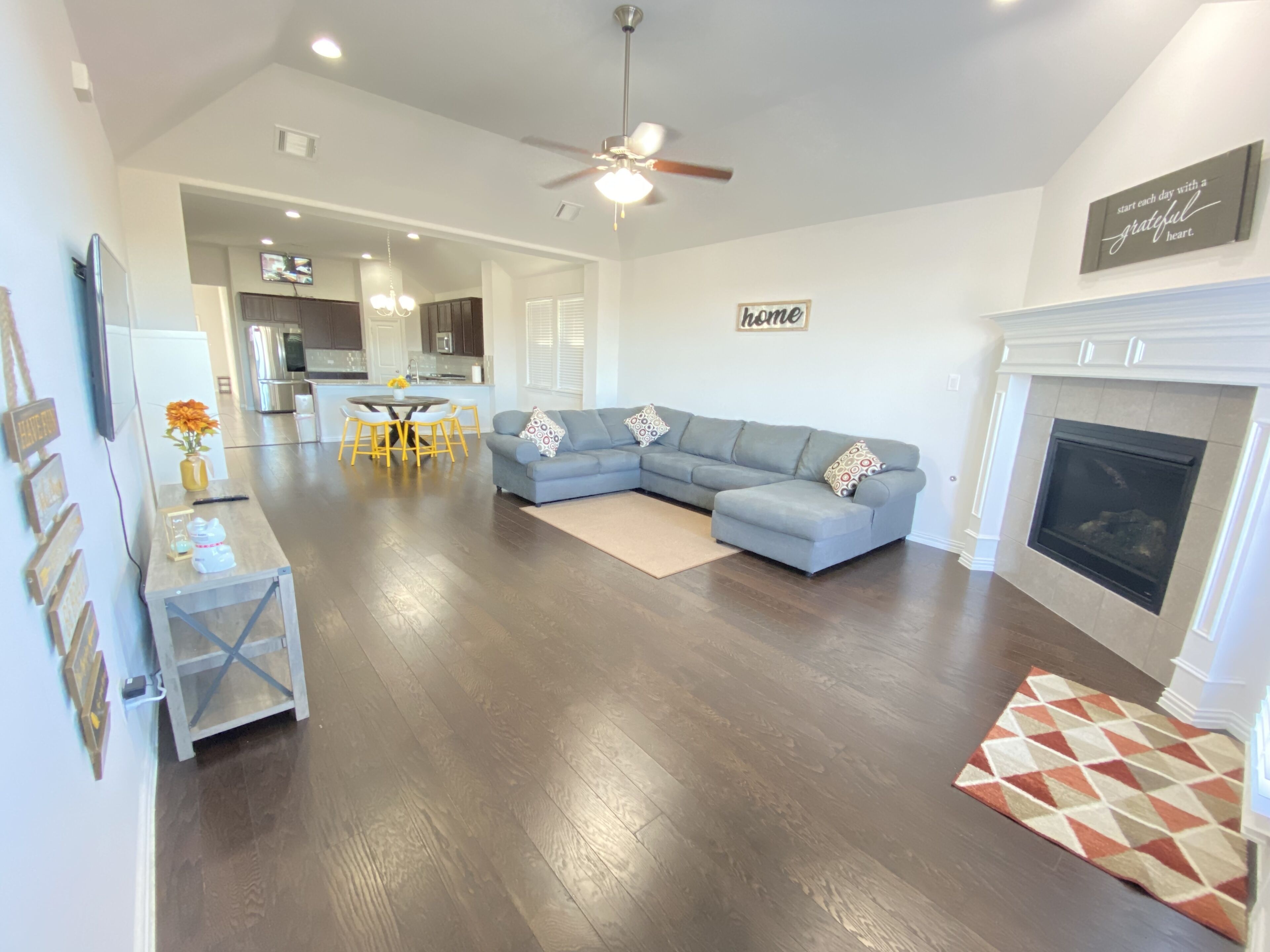 A spacious living room with a gray sectional sofa, a fireplace, and a dining area with yellow chairs.