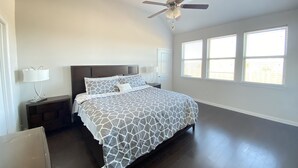 A bedroom with a bed, a ceiling fan, a nightstand, a lamp, and windows. - Beautiful Lake House in Garland Texas (Garland)