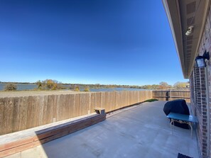 Une terrasse avec vue sur un lac, une clôture en bois et un barbecue.