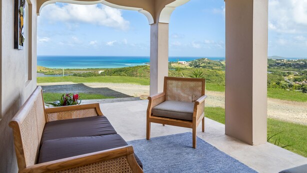 A covered outdoor seating area with a view of the ocean and landscape.