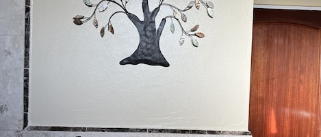 Une salle de bain avec un porte-serviettes fixé au mur, sur lequel est posée une serviette blanche, une fresque murale représentant un arbre décoratif et une porte en bois.