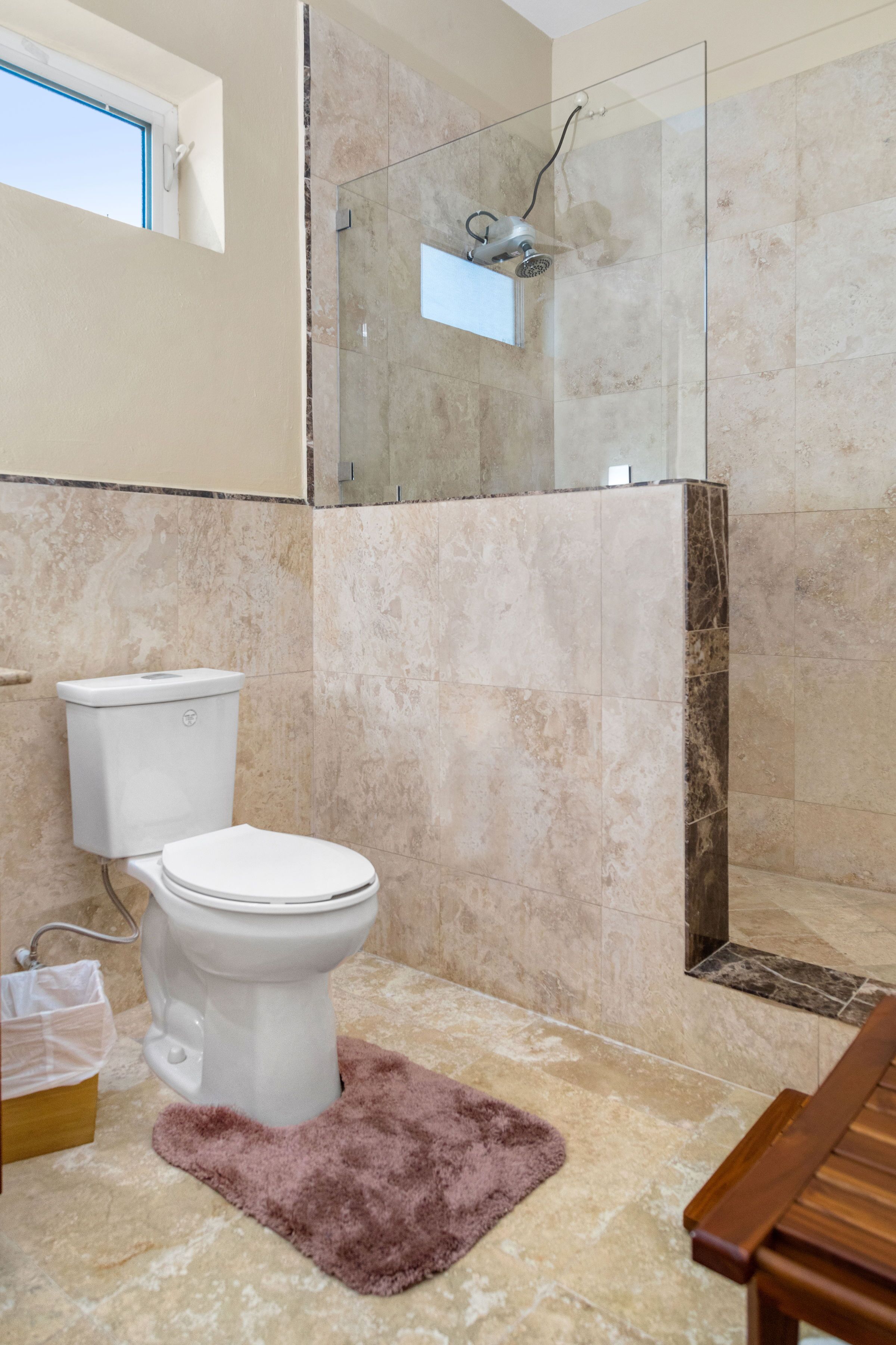 A bathroom with a toilet, a glass-enclosed shower, and a marble floor.