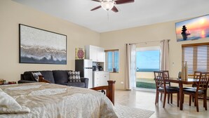 A spacious room with a bed, a dining table with chairs, a kitchen area, and a balcony with a view of the ocean.