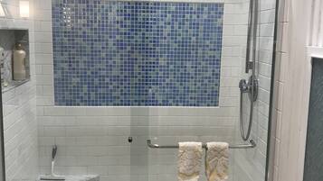 A glass-enclosed shower with a tiled wall, a marble shelf, and a towel rack.
