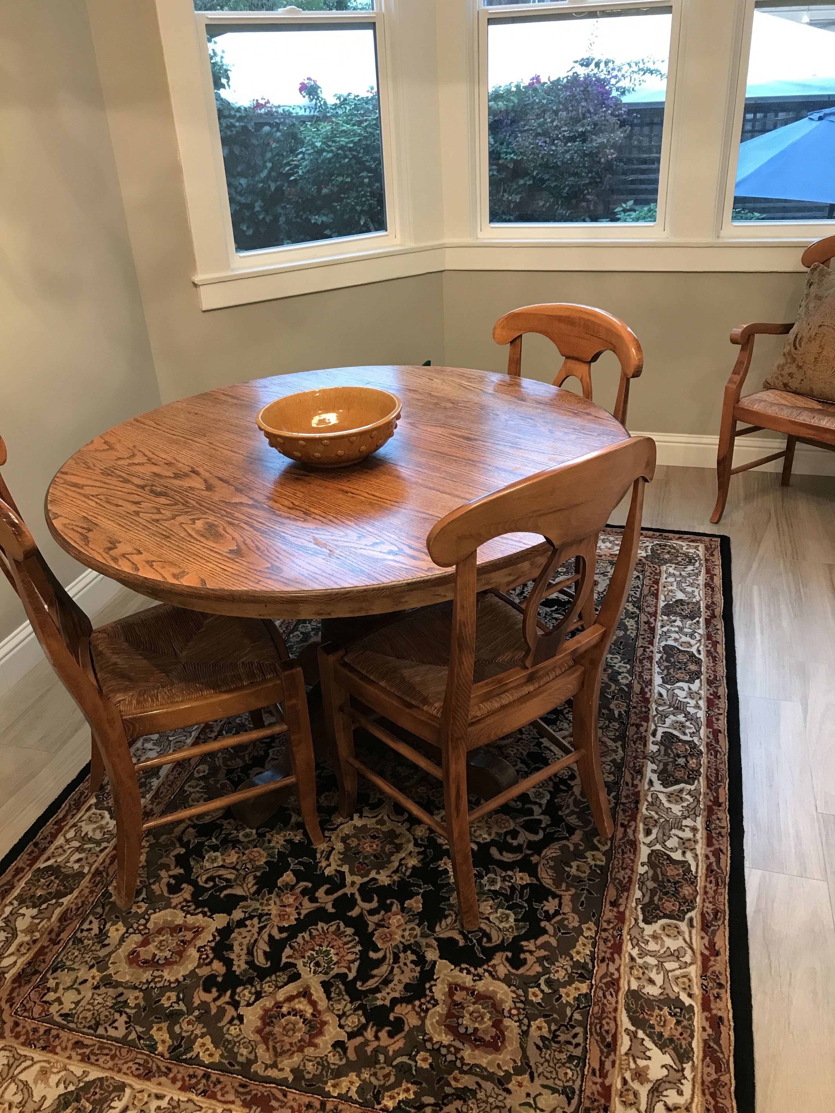 A round wooden dining table with a bowl on it, surrounded by wooden chairs with cushioned seats.