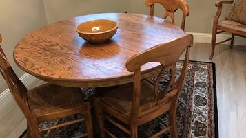 A round wooden dining table with a bowl on it, surrounded by wooden chairs with cushioned seats.