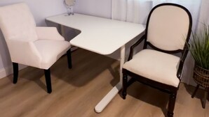 Una habitación con un escritorio blanco, dos sillas, un espejo redondo pequeño y una obra de arte con un caballito de mar en la pared.