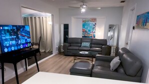 Una sala de estar moderna con un televisor de pantalla plana, un sofá, una mesita de centro y un pequeño bote de basura blanco.