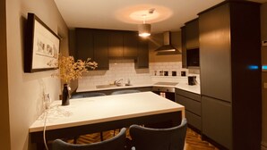 A modern kitchen with dark cabinets, a white countertop, and a central island with two chairs. - 3 BEDROOM APARTMENT BESIDE THE CASHEL PALACE HOTEL (Cashel)