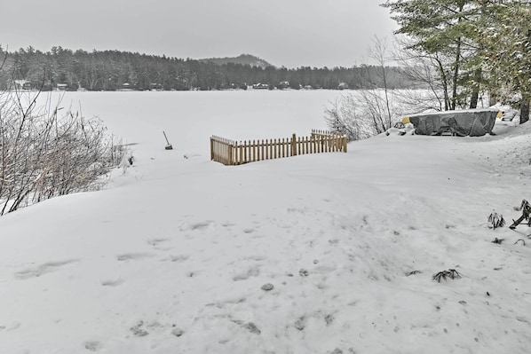 A snow-covered landscape with a wooden fence and a covered area, likely a cabin or shelter, near a body of water.
