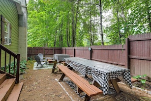An outdoor patio with picnic tables and chairs, surrounded by a wooden fence and trees.