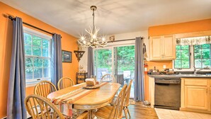 A dining area with a wooden table and chairs, a chandelier, and a view of the outdoors through large windows. - Rustic Adirondacks Home w/ Hot Tub & Lake Access! (Chestertown)