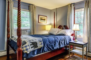 A four-poster bed with a quilt, a bedside table with a lamp, and a picture on the wall.