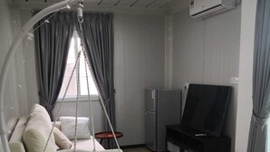 Ein gemütlicher Wohnraum mit Hängesessel, Flachbildfernseher, Kühlschrank und einem Streifenmuster-Teppich.