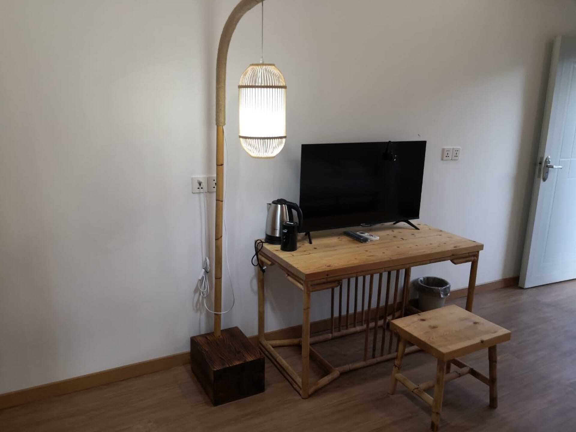 Una habitación pequeña con una mesa de madera, un televisor, un hervidor y un banco.