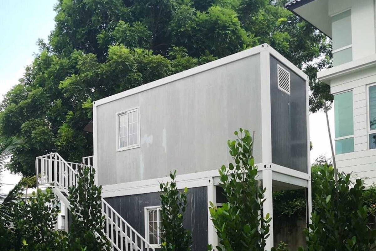 Un bâtiment moderne à deux étages, avec une façade grise, des éléments décoratifs blancs et un escalier blanc menant à l’entrée.