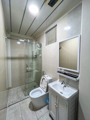 Un bagno con doccia vetro, toilette, lavandino e specchio.