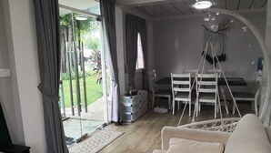 Ein modernes Wohnzimmer mit einer Couch, einem Esstisch mit Stühlen, einer kleinen Küchenzeile und Blick ins Freie.