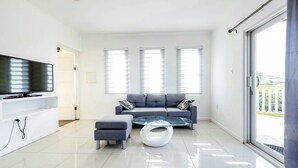 Un salon moderne avec un canapé gris, une table basse en verre et un téléviseur à écran plat posé sur une console blanche.